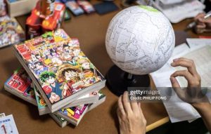 One Piece Manga - Manga novels sitting on a wooden desk with a global next to them and someone writing.